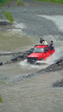 Su her yöne sıçrayıp Merapi Dağı eteğindeki lav turunda yolcuları ıslatana kadar yüksek hızda nehirden geçen bir off-road turist cipinin yavaş çekim görüntüleri.