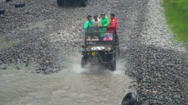 Endonezya 'nın Yogyakarta kentindeki Merapi Dağı eteğindeki lav turunda su her yöne sıçrayıp yolcuları ıslatana kadar yüksek hızda nehri geçen bir off-road turisti 4k görüntüsü.