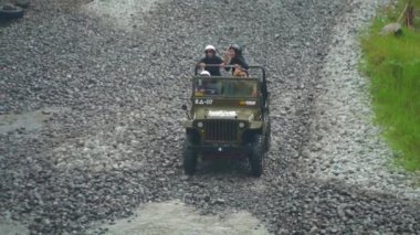 Endonezya 'nın Yogyakarta kentindeki Merapi Dağı eteğindeki lav turunda su her yöne sıçrayıp yolcuları ıslatana kadar yüksek hızda nehri geçen bir off-road turisti 4k görüntüsü.