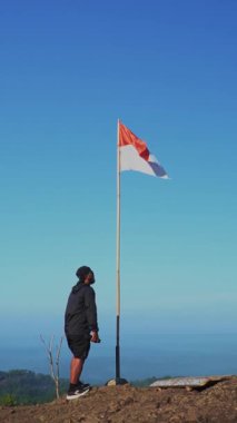 Bir adam, kırmızı ve beyaz Endonezya ulusal bayrağıyla antik Nglanggeran volkanının tepesine ulaşmayı başardı. Sallanan bayrağıyla kayalık bir dağın tepesinde yavaş hareket eden bir adam.
