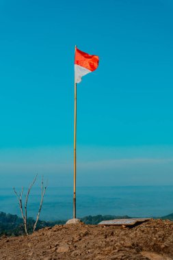 Antik Nglanggeran volkanının zirvesine kayalar hükmediyor ve kırmızı ve beyaz Endonezya bayrağını taşıyor. Tropikal bir sabah dalgalı bayrağıyla kayalık dağ zirvesinin fotoğrafı.