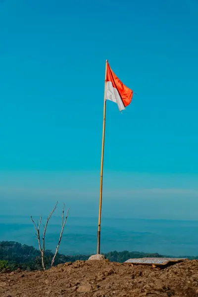 stock image The peak of the ancient volcano Nglanggeran is dominated by rocks and contains the red and white Indonesian flag. Photo of rocky mountain peak with waving flag on a tropical morning