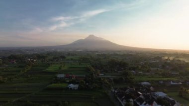 Dağ 'ın sabah güzel manzaralı 4K hava görüntüsü. Güneş doğduktan hemen sonra volkanın havadan manzarası. Önünde pirinç tarlaları ve yerleşim alanları var.