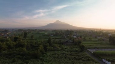Dağ 'ın sabah güzel manzaralı 4K hava görüntüsü. Güneş doğduktan hemen sonra volkanın havadan manzarası. Önünde pirinç tarlaları ve yerleşim alanları var.