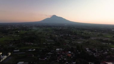 Merapi Dağı 'nın yaklaşık 12 mil uzaklıktaki 4K hava görüntüsü. Aktif bir volkanın sabah manzarası güneş doğduktan sonra, ön planda pirinç tarlaları ve yerleşim alanları ile birlikte.