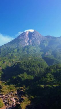 Merapi Dağı 'nın panoramik manzaralı, güzel bir yaz sabahı manzaralı hava aracı uçuş videosu. Önünde yeşil bir orman olan etkin bir volkanın 4k manzarası.