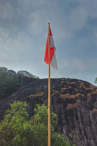 stock image The peak of the ancient volcano Nglanggeran is dominated by rocks and contains the red and white Indonesian flag. Photo of rocky mountain peak with waving flag on a tropical morning