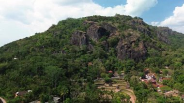 Gün boyunca Nglanggeran Antik Volkan eko eko alanının 4k hava görüntüsü. Güzel bir kırsal bölgedeki yemyeşil ağaçlarla çevrili antik kaya tepelerinin hava görüntüleri.