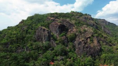 Gün boyunca Nglanggeran Antik Volkan eko eko alanının 4k hava görüntüsü. Güzel bir kırsal bölgedeki yemyeşil ağaçlarla çevrili antik kaya tepelerinin hava görüntüleri.