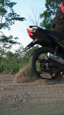 Motosikletin arka tekeri kumda yavaşça kayıyor. Motosikletlinin kumlu bir yolda sıkıştığı ve tekerleklerin altından kum uçana kadar gazı çekmeye çalıştığı görüntüler..