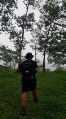 Asyalı yetişkin bir adamın şortu, tişörtü ve şapkasıyla vahşi doğada yürüyüşünün görüntüsü. Erkek bir maceracı ormanda tek başına çeşitli sarp araziler ve yoğun otlar arasında yürür.