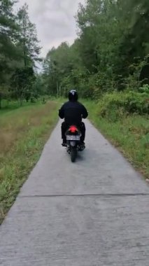 Yoğun bir çam ormanında siyah bir motosiklet kullanan bir motorcunun portre görüntüleri. Motosiklet sürücüsü güzel manzaralı sessiz bir çam ormanında hızla ilerliyordu.