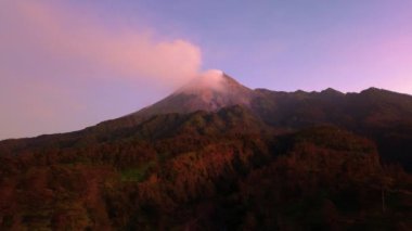 Güneş doğarken Merapi Dağı 'nın 4k hava görüntüsü. Yazın güzel manzaralı yakın mesafeden. Sabah volkanın havadan manzarası. Önünde orman ve yeşil tepeler.