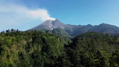 Sabah Merapi Dağı 'nın 4k hava görüntüsü yaz sabahları güzel manzaralı yakın mesafeden. Önünde orman ve yeşil tepeler olan volkanın havadan manzarası.