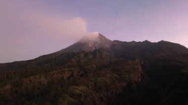 Güneş doğarken Merapi Dağı 'nın 4k hava görüntüsü. Yazın güzel manzaralı yakın mesafeden. Sabah volkanın havadan manzarası. Önünde orman ve yeşil tepeler.