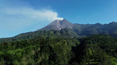 Sabah Merapi Dağı 'nın 4k hava görüntüsü yaz sabahları güzel manzaralı yakın mesafeden. Önünde orman ve yeşil tepeler olan volkanın havadan manzarası.