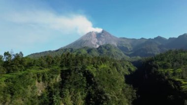 Sabah Merapi Dağı 'nın 4k hava görüntüsü yaz sabahları güzel manzaralı yakın mesafeden. Önünde orman ve yeşil tepeler olan volkanın havadan manzarası.