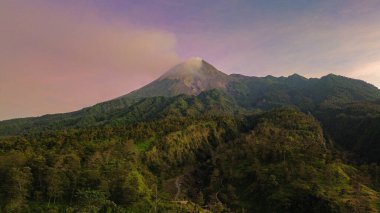 Güneş doğarken Merapi Dağı 'nın manzarası çok güzeldir. Önünde mor bir gökyüzü, ormanı ve vadisi olan aktif bir volkanın detaylı manzarası.