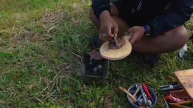Maceracı ellerinin kömür briketlerini kullanarak bifteği kızartışını yakından çek. Basit ekipman ve malzemelerle doğada yemek ve yemek pişirme kavramı..
