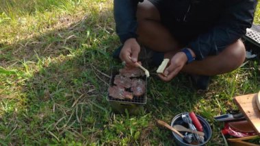 Maceracı ellerinin kömür briketlerini kullanarak bifteği kızartışını yakından çek. Basit ekipman ve malzemelerle doğada yemek ve yemek pişirme kavramı..