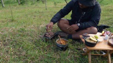 Maceracı ellerinin kömür briketlerini kullanarak bifteği kızartışını yakından çek. Basit ekipman ve malzemelerle doğada yemek ve yemek pişirme kavramı..