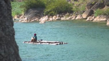 Yaşlı bir kadın bambu salıyla kayalık kayalıklarla çevrili temiz bir nehri geçiyor. Nehir bölgesinde güzel panoramayla bambu sallara binen insanların 4k görüntüsü.