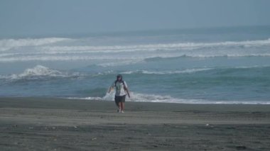 Rüzgarlı bir plajın kenarında kumsalda yürüyen yalnız bir maceracının görüntüsü. Bir erkek gezgin kumsalda tek başına yürüyor.