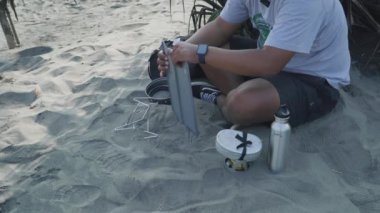 Bushcraft konsepti doğada basit aletler ve malzemelerle kumsalda yemek pişirmek ve yemek yapmaktır. Bir maceraperest sahilde köfte ve sosis pişiriyor.