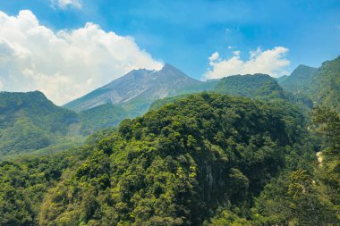 Gündüz vakti aktif volkanın yakın çekim manzarası. Yogyakarta, Endonezya 'daki Merapi Dağı ön planda bir tepe ve arka planda bulutlu bir gökyüzü ile yakından bakıldığında gerçekten büyüleyici.