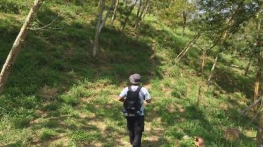 Tek başına maceraperest bir sırt çantası taşıyarak güzel ve yeşil ormanda yürür. Asyalı yetişkin bir erkek maceracı sık bir ormanın ortasında kamp yapmak ve çalı çırpmak için tek başına yürüyüş yapıyor.