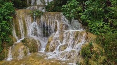 Hala hızlı akan suyla doğal ve güzel olan bir şelalenin video görüntüleri. Kayaların hakim olduğu dramatik bir şelalenin ve etrafındaki yoğun ağaçların temiz su akışının 4k görüntüleri.