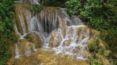 Hala hızlı akan suyla doğal ve güzel olan bir şelalenin video görüntüleri. Kayaların hakim olduğu dramatik bir şelalenin ve etrafındaki yoğun ağaçların temiz su akışının 4k görüntüleri.