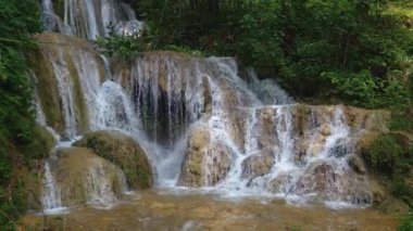 Hala hızlı akan suyla doğal ve güzel olan bir şelalenin video görüntüleri. Kayaların hakim olduğu dramatik bir şelalenin ve etrafındaki yoğun ağaçların temiz su akışının 4k görüntüleri.