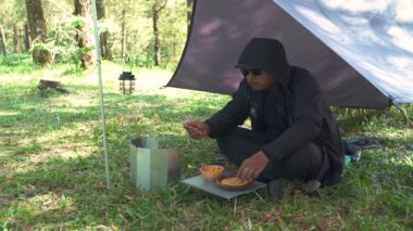 Roti Canai ile köri pişirirken çam ormanlarında tek başına kamp yapma fikri. Asyalı bir erkek maceracı, güzel doğada yemek pişirip hazırlanırken tek başına kamp yapar.