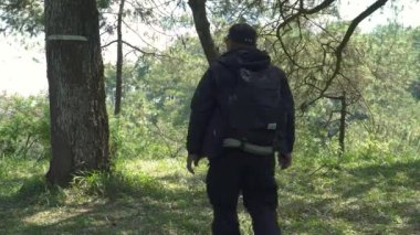 Solo Hiker sırtında bir sırt çantasıyla çeşitli arazilerle vahşi doğada yürür. Asyalı erkek maceracı ormanın ortasında tek başına, yemyeşil ağaçlar ve kalın yeşil otlar arasında yürüyor.