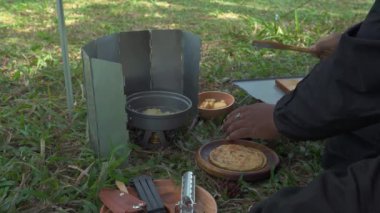 Roti Canai ile köri pişirirken çam ormanlarında tek başına kamp yapma fikri. Asyalı bir erkek maceracı, güzel doğada yemek pişirip hazırlanırken tek başına kamp yapar.