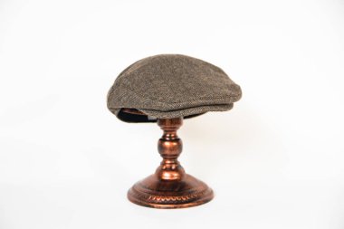 Detail of a scally cap or flat hat or herringbone wool fabric hat mounted on a bronze mannequin head with a white background. Concept photo of a classic dark khaki hat on an elegant bronze mannequin clipart