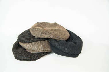 Pile of newsboy hats and scally caps with assorted different colors and patterns on a white background. Concept photo of stack of classic irish hats in white studio clipart