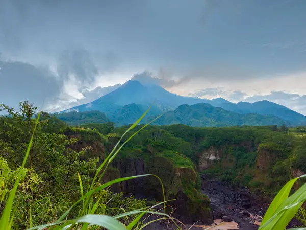 Merapi Dağı 'nın panorama' sı, öğleden sonra bulutların etrafını sardığı yakın bir mesafeden. Önünde kayalar ve vadi olan güneyden aktif volkan manzarası.