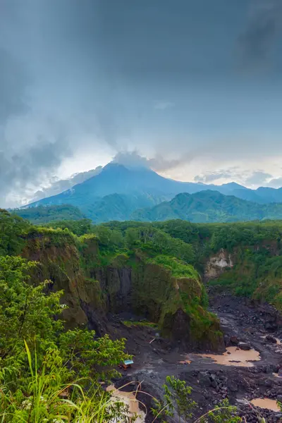 Merapi Dağı 'nın panorama' sı, öğleden sonra bulutların etrafını sardığı yakın bir mesafeden. Önünde kayalar ve vadi olan güneyden aktif volkan manzarası.