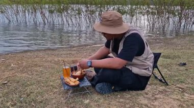 Erkek bir maceraperest, rezervuarın kenarında köfteli tavuklu erişte pişiriyor. Gölün kenarında kamp yapmak ve basit ekipmanlarla yemek pişirmek.