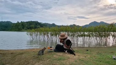 Bir erkek maceracı, su deposunun kenarında tavuk köfteli erişte yer ve iki aç vahşi kedi ona eşlik eder. Vahşi kedilerle gölün kenarında kamp yapma fikri.