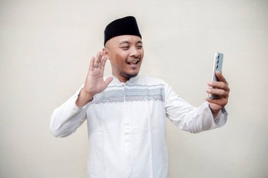 Müslüman kıyafetleri içinde Asyalı bir adam ve Peci, memleketine dönemediği için Kurban Bayramı 'nda video çağrısı yapıyor. Müslüman adamın beyaz arka planda izole edilmiş görüntüler yaptığı yakın plan görüntüleri.