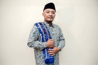 Müslüman temalı, bronzlaşmış Asyalı bir adamın desenli gömlek ya da batik desenli gömlek giydiği, omuzlarına siyah başlık taktığı ve beyaz arka planda çeşitli pozlar verdiği bir konsept fotoğraf..