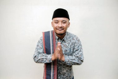 Müslüman temalı, bronzlaşmış Asyalı bir adamın desenli gömlek, siyah başlık ve sarong giymiş beyaz arka planda çeşitli pozlar verirken çekilmiş konsept fotoğrafı..