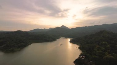 Gün batımında gökyüzü sararırken Endonezya, Yogyakarta 'daki Sermo Reservoir' ın hava görüntüleri. İnsansız hava aracı manzarası güzel, temiz gölü gösteriyor. Arka planda yemyeşil ağaçlar ve tepeler var.