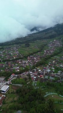 Dağın eteklerinden, pirinç tarlaları ve birkaç güzel ve serin köyle 4K hava görüntüsü. Merapi Dağı eteğinde köy bölgesinin hava manzarası ve yeşil pirinç tarlaları.