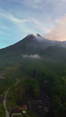 Önünde sık bir orman manzarası olan aktif bir volkanın sabahki havadan görüntüsü. Drone görüntüleri, güneş doğarken Sleman, Yogyakarta, Endonezya 'daki Merapi Dağı' nın güzelliğini gösteriyor.