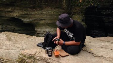 Erkek bir maceracı nehir kıyısındaki antik kayalarda baharatlı çay yapmak için su kaynatır. Bushcraft konsepti, volkanik lavlardan antik kayalarda sıcak çay yaparak doğanın huzurunun tadını çıkarmaktır..