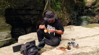 Erkek bir maceracı nehir kıyısındaki antik kayalarda baharatlı çay yapmak için su kaynatır. Bushcraft konsepti, volkanik lavlardan antik kayalarda sıcak çay yaparak doğanın huzurunun tadını çıkarmaktır..